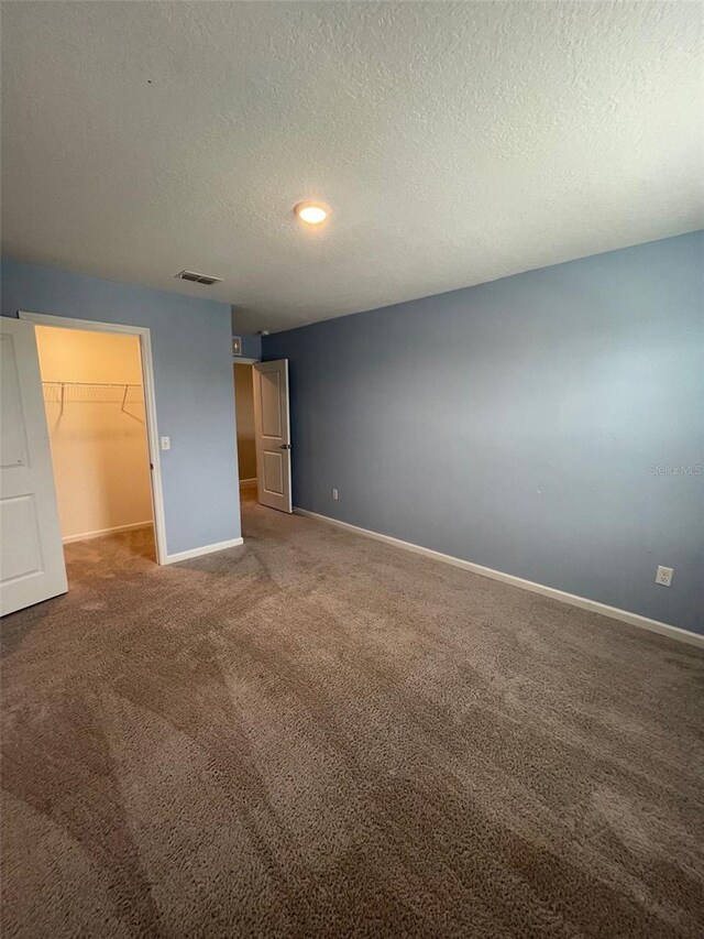 unfurnished bedroom with a walk in closet, a closet, carpet floors, and a textured ceiling