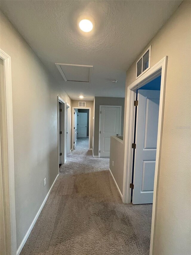 corridor with light carpet and a textured ceiling