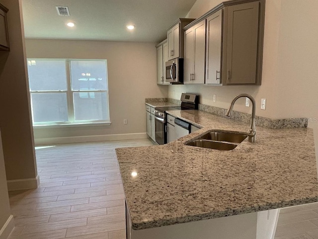 kitchen with sink, light wood-type flooring, appliances with stainless steel finishes, light stone counters, and kitchen peninsula