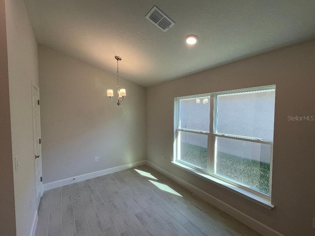 spare room featuring light hardwood / wood-style floors, vaulted ceiling, and a notable chandelier