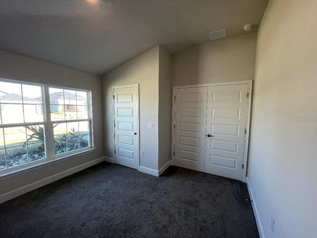 unfurnished bedroom with vaulted ceiling, dark carpet, and a closet