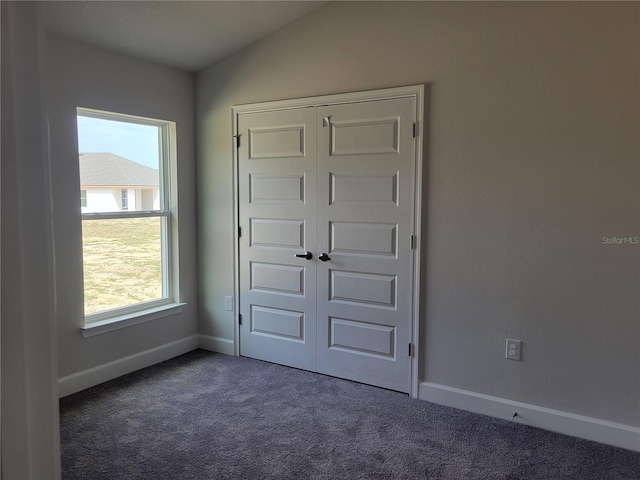 unfurnished bedroom featuring dark colored carpet, a closet, vaulted ceiling, and multiple windows