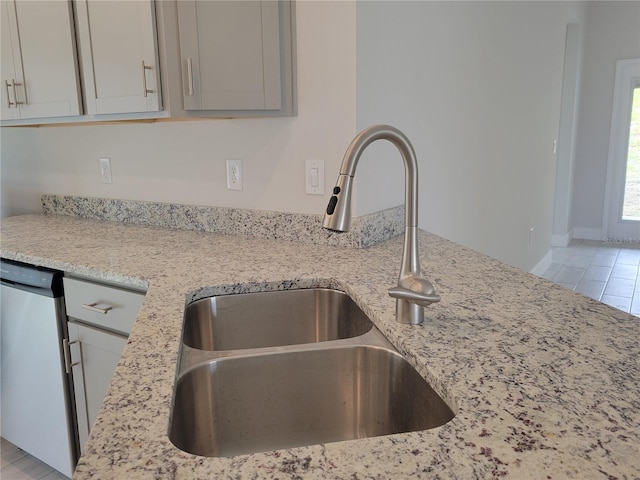 kitchen featuring dishwasher, light stone counters, and sink