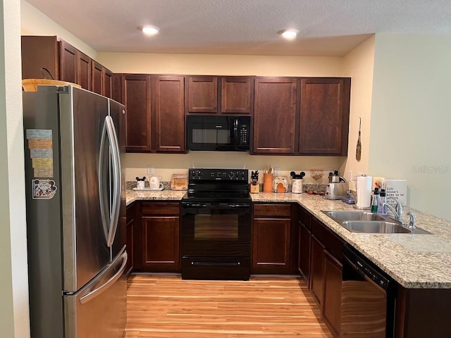 kitchen featuring light stone counters, black appliances, light wood-type flooring, sink, and a textured ceiling