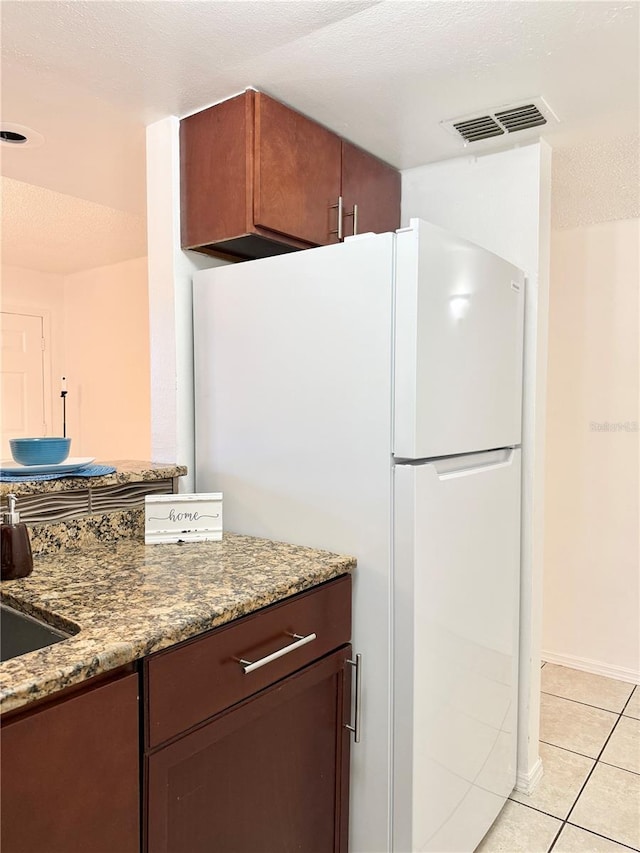 kitchen featuring light tile patterned flooring, dark stone counters, white fridge, and a textured ceiling