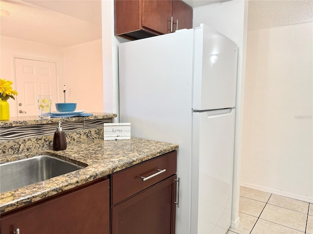 kitchen featuring sink, dark stone countertops, white refrigerator, light tile patterned floors, and a textured ceiling