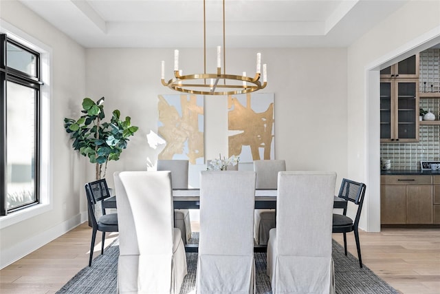 dining area featuring a raised ceiling, a notable chandelier, and light hardwood / wood-style flooring