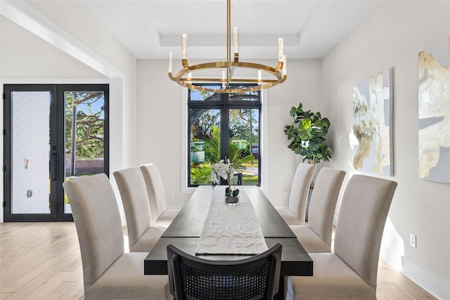 dining room featuring light hardwood / wood-style floors, french doors, an inviting chandelier, and a raised ceiling