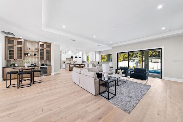 living room with french doors, beverage cooler, a tray ceiling, and light hardwood / wood-style flooring