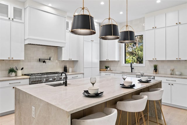 kitchen featuring white cabinets, a kitchen island with sink, light stone countertops, and sink