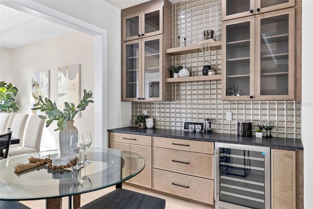 bar featuring light brown cabinets, beverage cooler, and backsplash