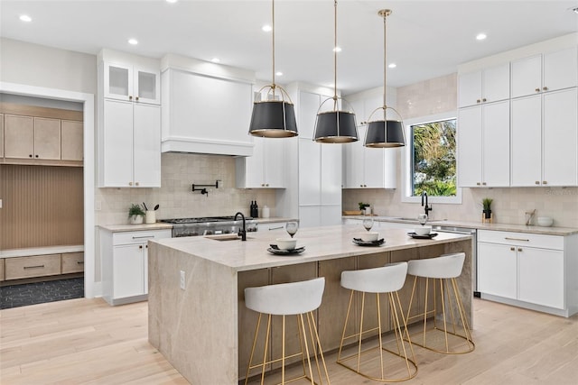 kitchen featuring white cabinets, sink, light stone countertops, and a center island with sink