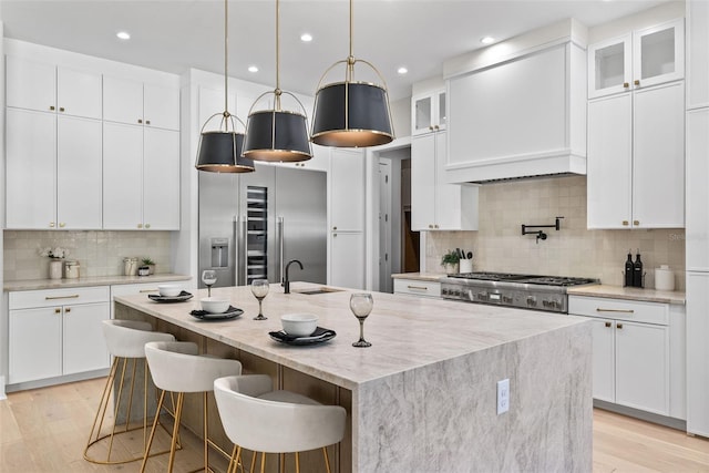 kitchen with white cabinets, a kitchen island with sink, custom exhaust hood, and decorative backsplash