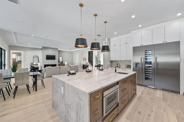 kitchen featuring light stone countertops, built in appliances, white cabinets, and an island with sink