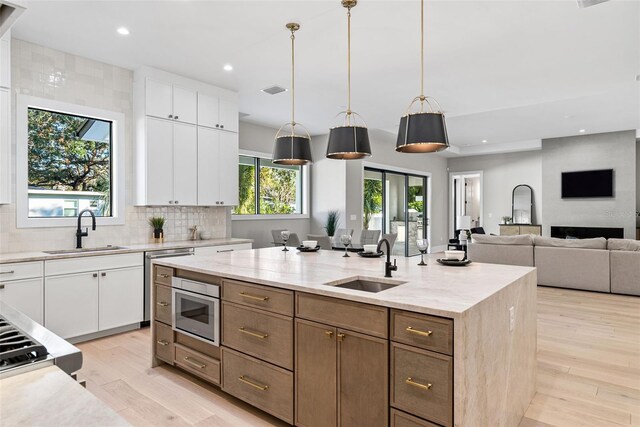 kitchen with sink, white cabinetry, a center island with sink, and stainless steel microwave