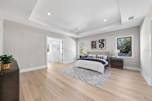 bedroom with light hardwood / wood-style floors and a tray ceiling