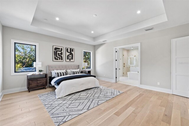 bedroom featuring ensuite bathroom, a raised ceiling, and multiple windows