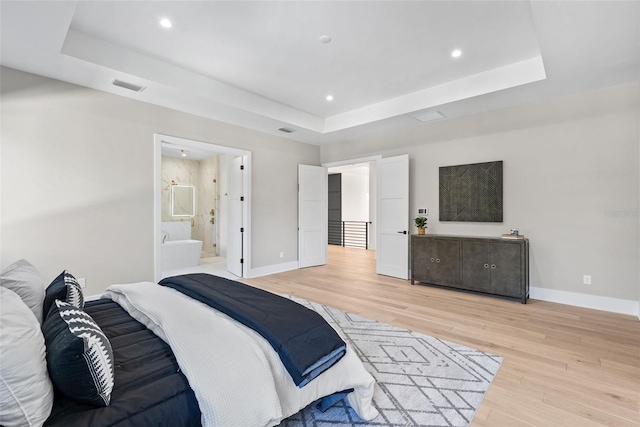 bedroom with light wood-type flooring, connected bathroom, and a raised ceiling