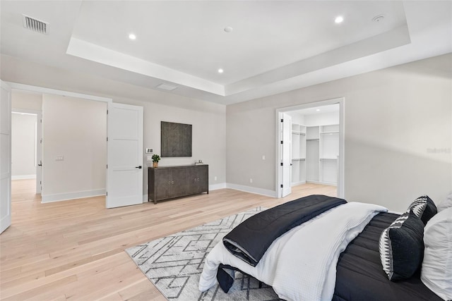 bedroom with a walk in closet, a raised ceiling, a closet, and light wood-type flooring