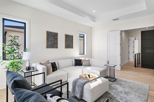 living room with a raised ceiling, a wealth of natural light, and hardwood / wood-style flooring