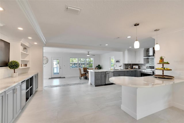 kitchen featuring kitchen peninsula, wall chimney exhaust hood, gray cabinetry, stainless steel appliances, and pendant lighting