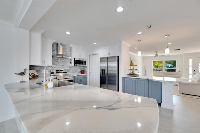 kitchen with kitchen peninsula, appliances with stainless steel finishes, wall chimney exhaust hood, white cabinets, and hanging light fixtures