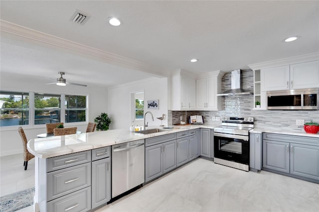 kitchen featuring wall chimney range hood, gray cabinets, appliances with stainless steel finishes, a healthy amount of sunlight, and kitchen peninsula