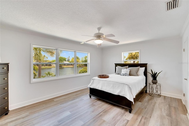 bedroom featuring ceiling fan, crown molding, a textured ceiling, a water view, and light wood-type flooring