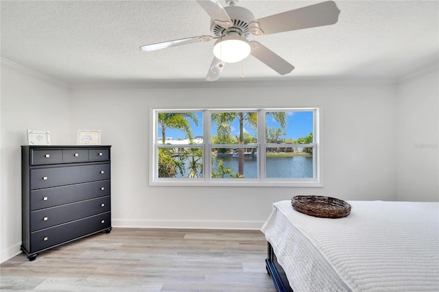 bedroom featuring a water view, light hardwood / wood-style flooring, ceiling fan, ornamental molding, and a textured ceiling