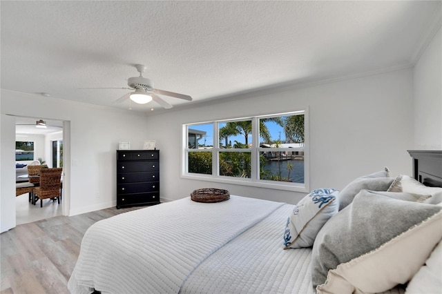 bedroom featuring ornamental molding, a textured ceiling, ceiling fan, a water view, and light hardwood / wood-style floors