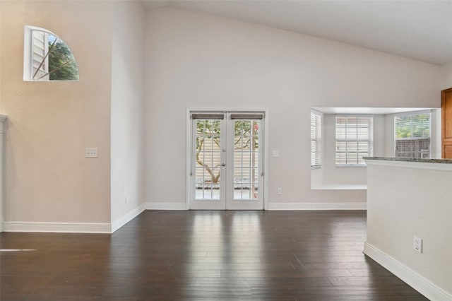 unfurnished living room with plenty of natural light, high vaulted ceiling, dark hardwood / wood-style floors, and french doors