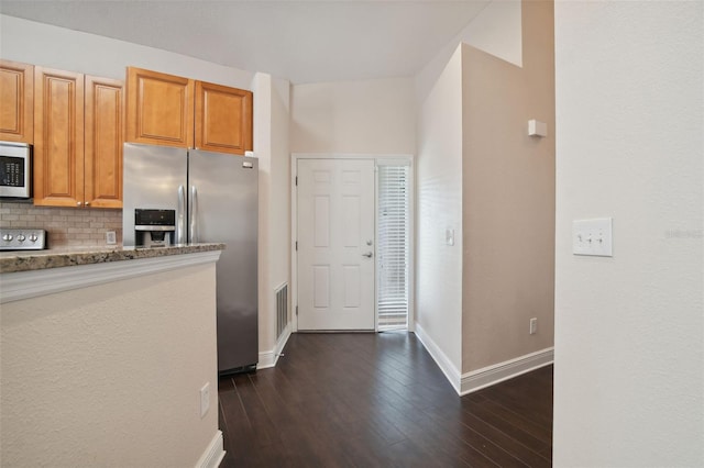 kitchen with light stone countertops, backsplash, stainless steel appliances, and dark wood-type flooring