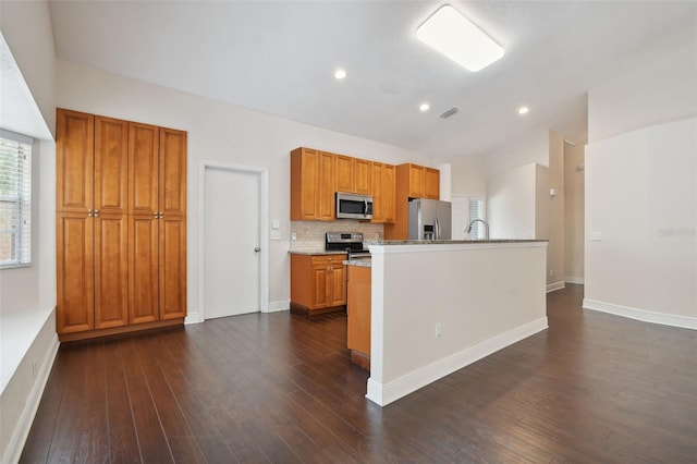 kitchen featuring dark wood-type flooring, stainless steel appliances, light stone counters, decorative backsplash, and a center island with sink