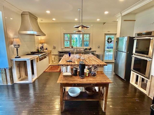 kitchen with dark hardwood / wood-style flooring, ornamental molding, wall chimney range hood, and appliances with stainless steel finishes