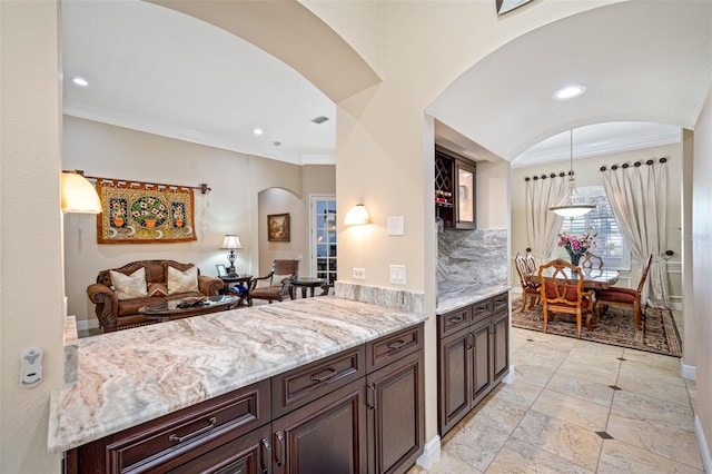 kitchen featuring crown molding, hanging light fixtures, light stone countertops, tasteful backsplash, and dark brown cabinetry