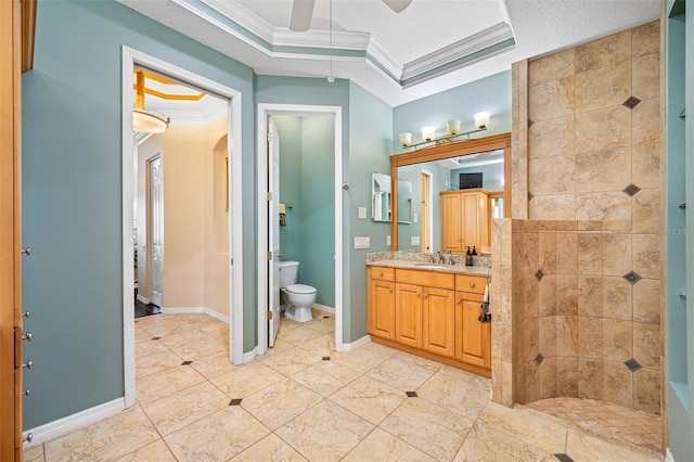 bathroom featuring a tile shower, vanity, ceiling fan, crown molding, and toilet