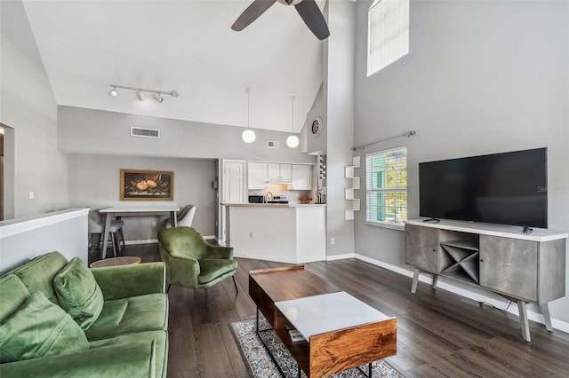 living room with a high ceiling, ceiling fan, track lighting, and dark wood-type flooring