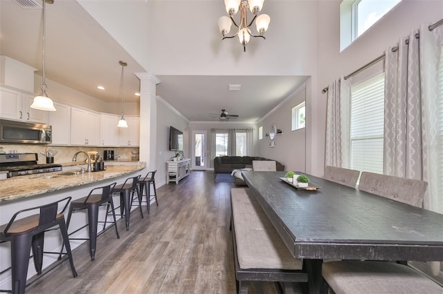 dining space featuring dark hardwood / wood-style flooring, decorative columns, ceiling fan with notable chandelier, crown molding, and sink