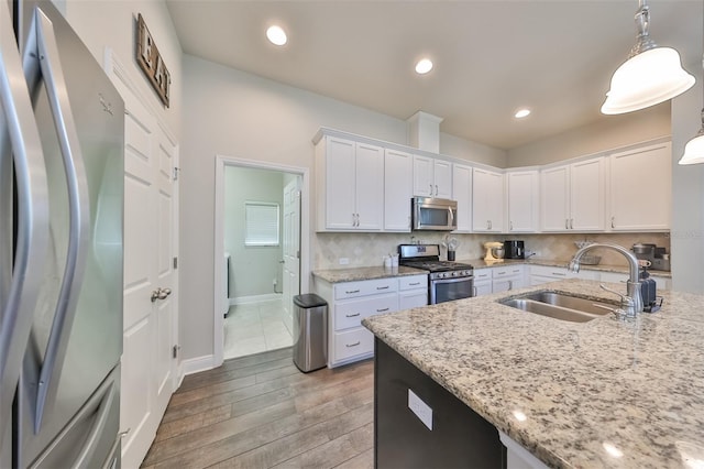 kitchen with white cabinetry, sink, hanging light fixtures, stainless steel appliances, and light stone counters