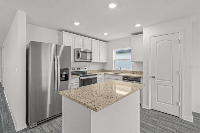 kitchen with a center island, white cabinetry, stainless steel appliances, light wood finished floors, and a sink