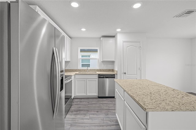 kitchen featuring a kitchen island, stainless steel appliances, sink, white cabinets, and light hardwood / wood-style floors