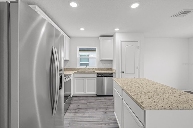 kitchen with visible vents, a center island, white cabinets, a sink, and appliances with stainless steel finishes