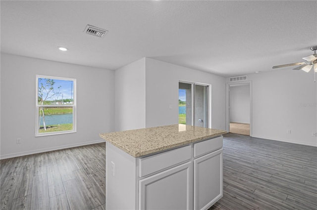 kitchen featuring a textured ceiling, a center island, white cabinets, dark wood-type flooring, and light stone counters