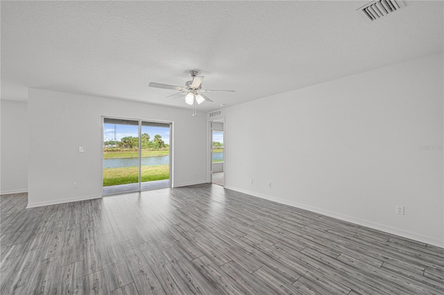 empty room with a textured ceiling, a water view, light wood-type flooring, and ceiling fan