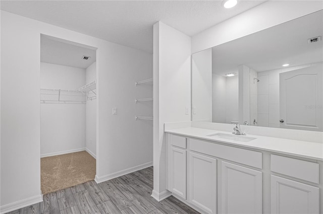 bathroom featuring tiled shower, vanity, visible vents, wood finished floors, and a walk in closet