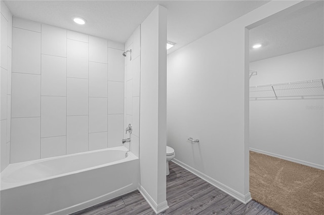 bathroom featuring toilet, a textured ceiling, tiled shower / bath combo, and wood-type flooring