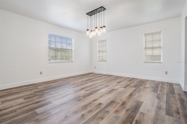 empty room featuring a notable chandelier, baseboards, and wood finished floors