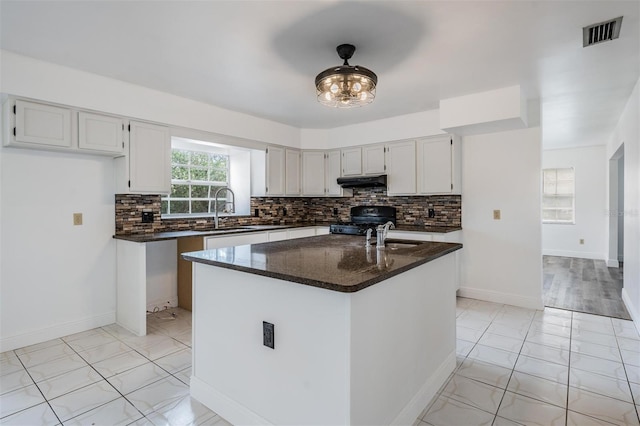 kitchen with visible vents, black gas stove, under cabinet range hood, decorative backsplash, and a sink