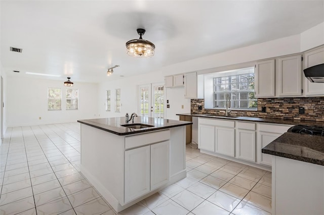 kitchen featuring decorative backsplash, a center island with sink, visible vents, and a sink