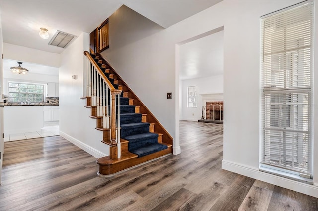 staircase with visible vents, a brick fireplace, baseboards, and wood finished floors